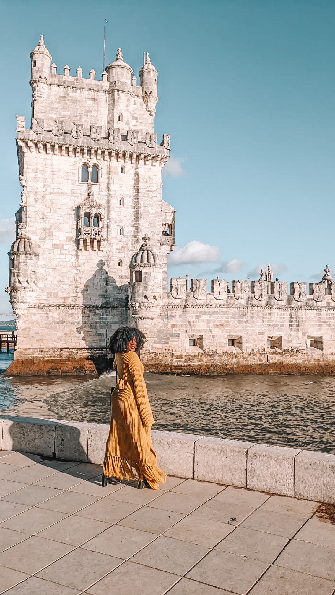Black woman with curly hair standing in front of the Belem Tower