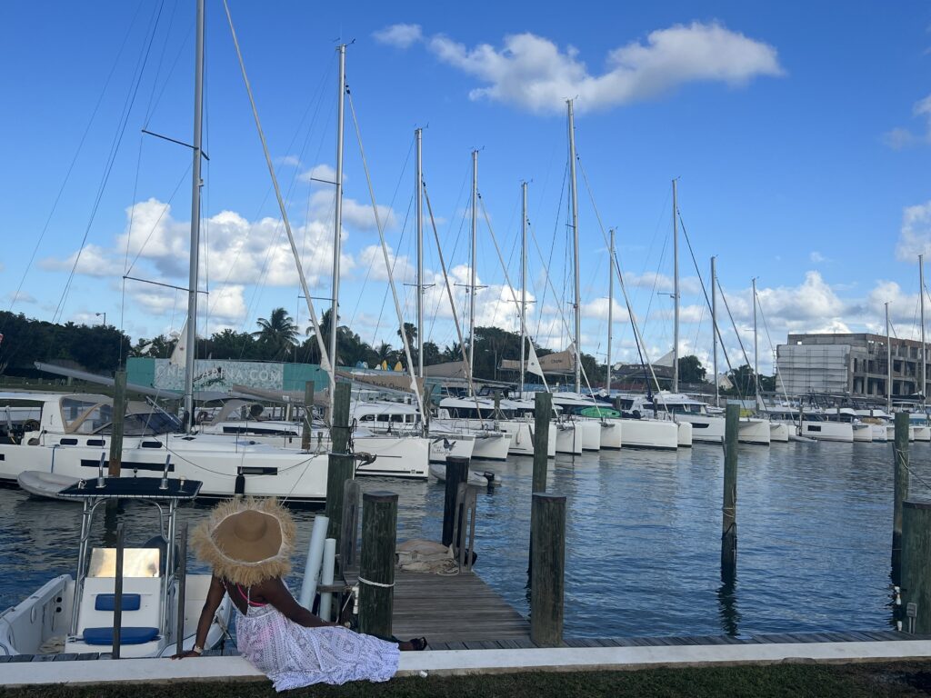woman in white dress and big brown sunhat staring out at the pier with lots of boats