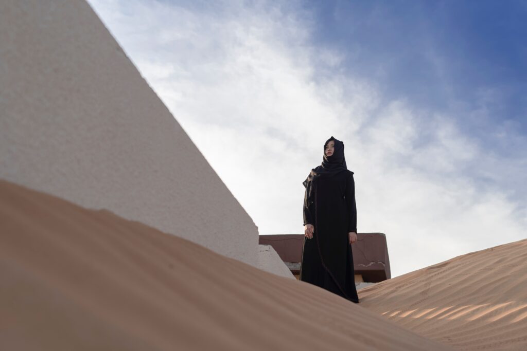 asian woman wearing a black abaya and black hijab in a sandy location