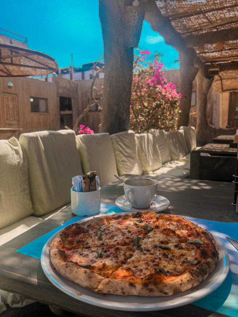 pan of margarita cheese pizza on table with Egyptian style hotel in the background. Located at at Eldorado Lodge and Restaurant in Dahab
