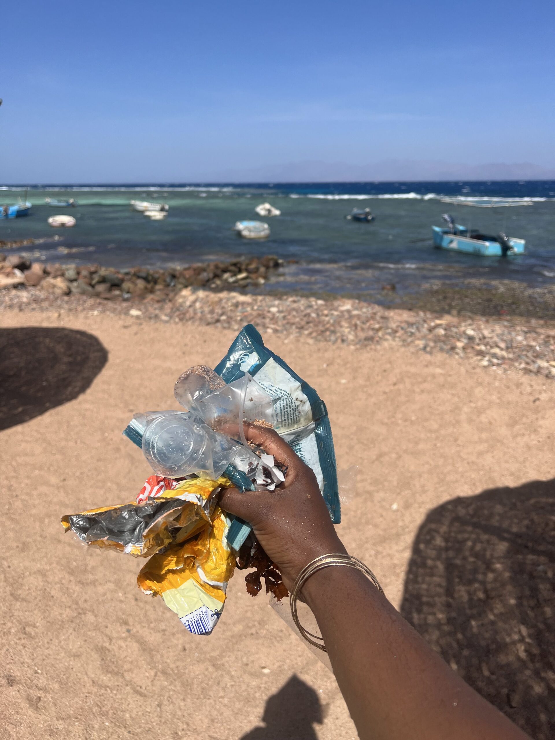 black woman's arm holding on to plastic trash on Dahab beach. The purpose is to support sustainable travel.
