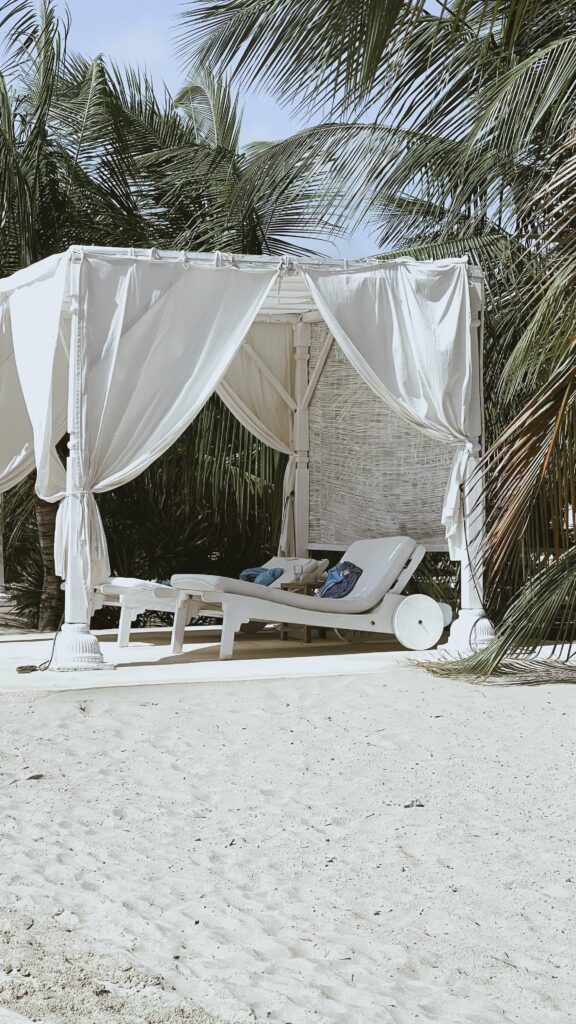 two sun chairs under a gazebo on white sand beach