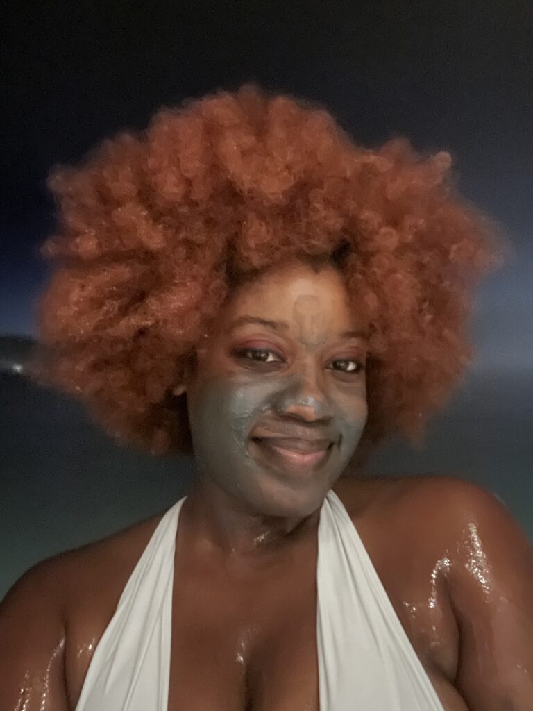 Black woman with ginger afro with black mud on her face at the Blue Lagoon