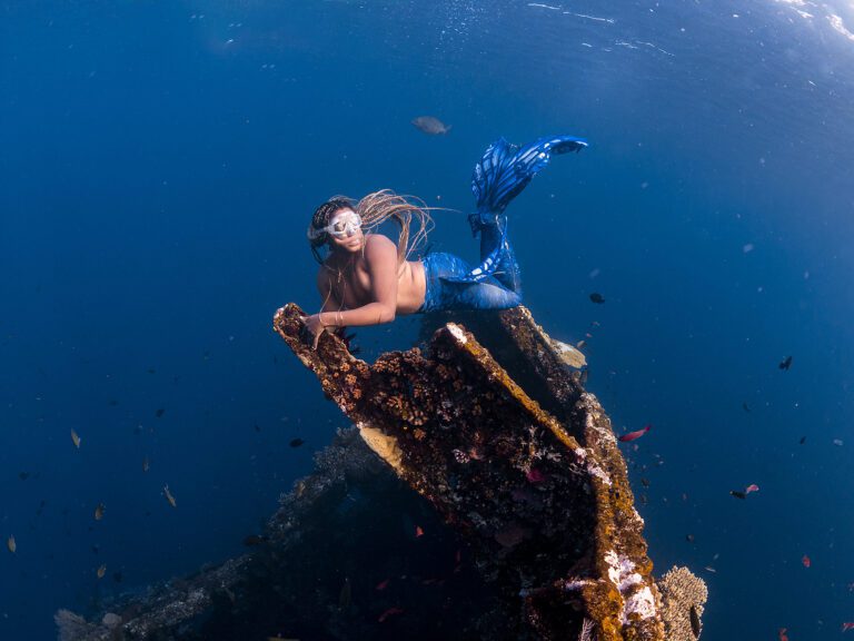 Black mermaid with blonde braids holding on to a shipwreck underwater in Amed Bali