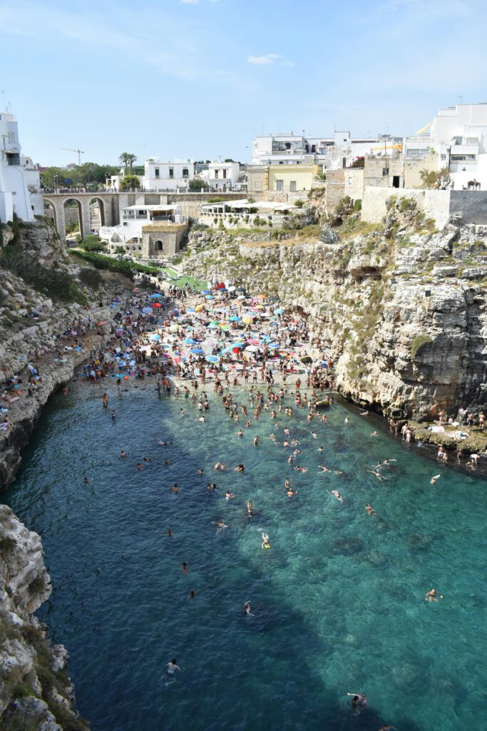 Drone shot of a beach in polignano a mare italy. Lots of people are in the water and on the sane