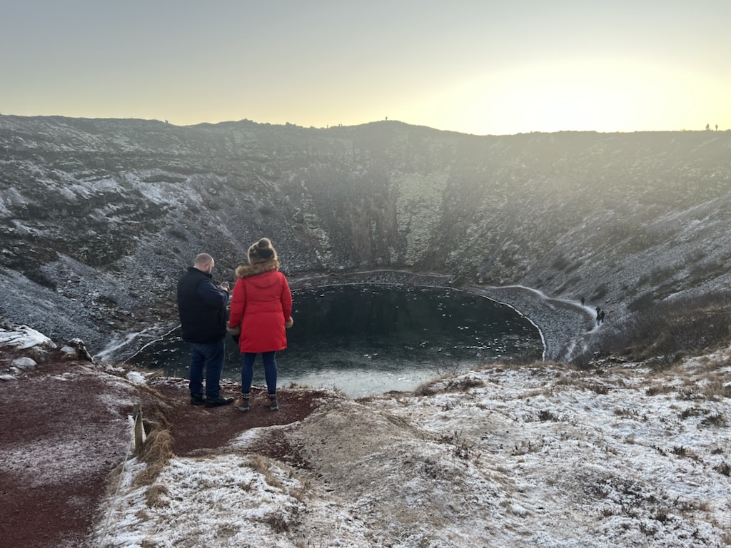 Kerid Crater at dusk. A male and female couple are looking out onto the crater. Light snow is on the ground