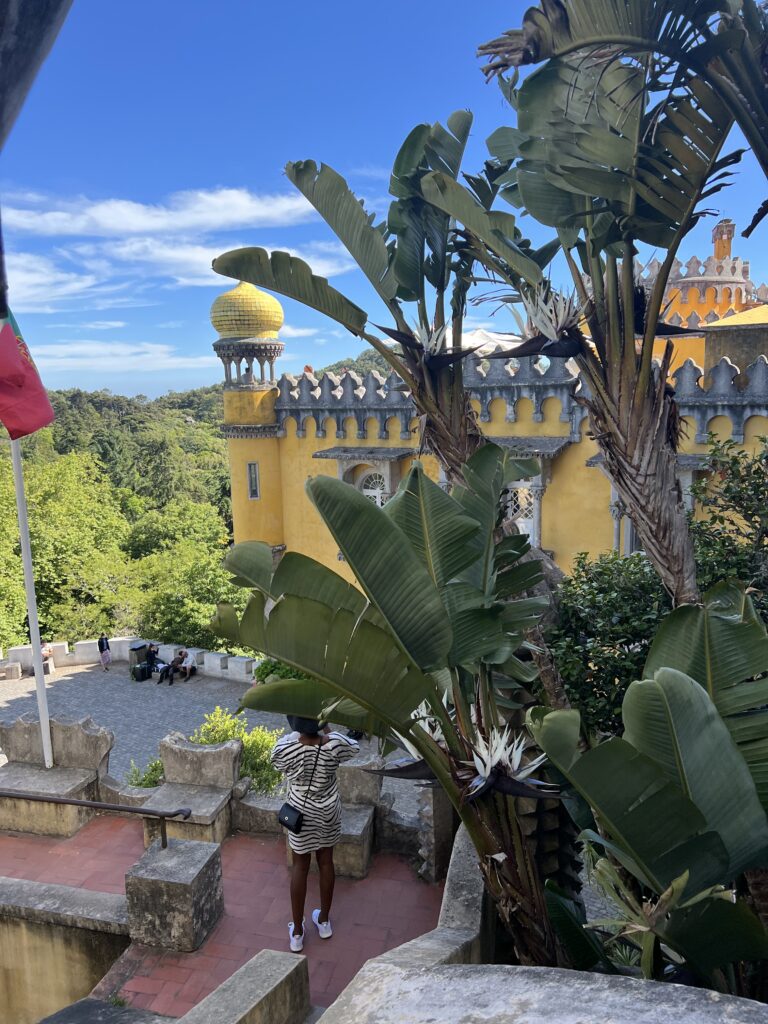 Sintra Palace is yellow with a few towers and lots of palm trees around it 