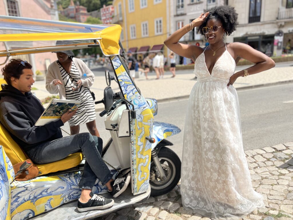 Black woman with afro posing in front of a rickshaw in Sintra Portugal while her friend talks. with the driver