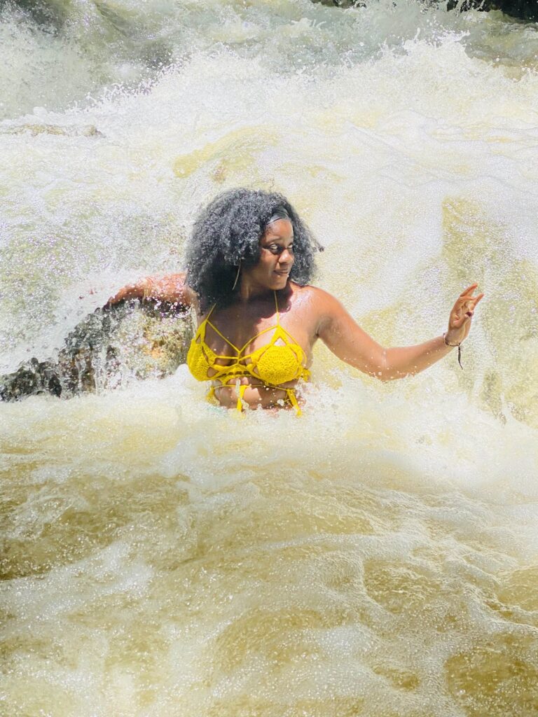 brown skinned Black woman with kinky hair in yellow crochet bathing suit in freshwater in Jamaica