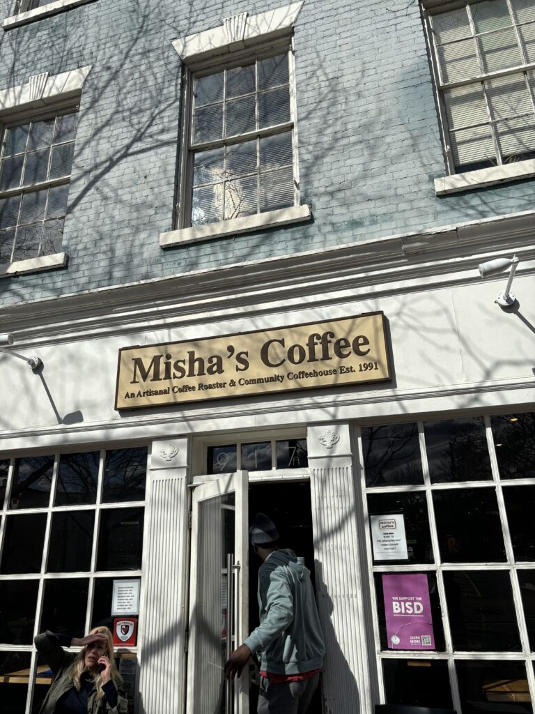storefront sign saying Misha's Coffee with a Black man with hat walking inside door