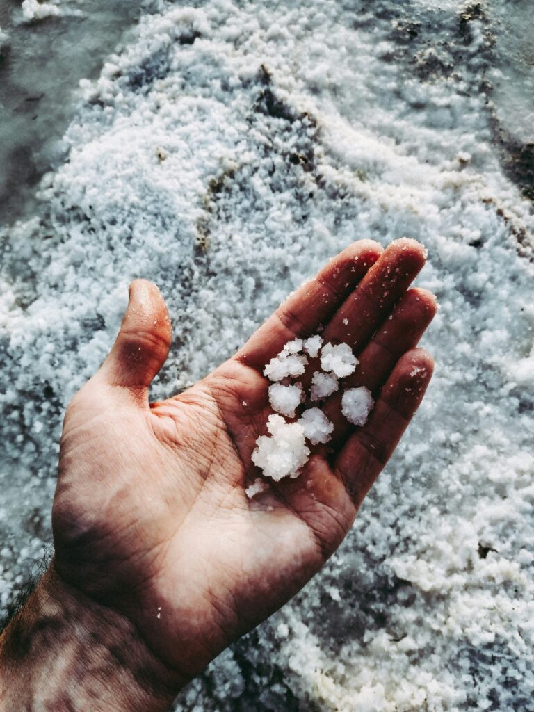 white hand holding clusters of salt. Background is a pile or raw salt 