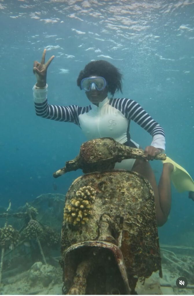 Black woman sitting on an underwater scooter throwing up a peace sign 