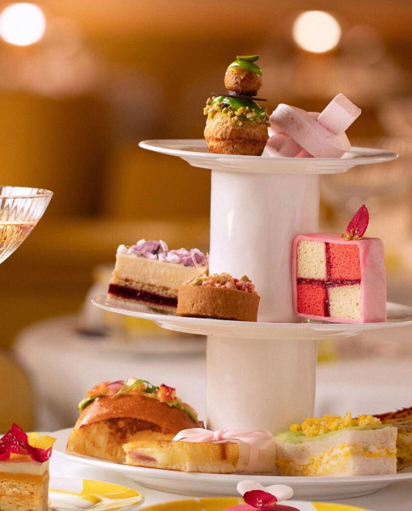 a three layer afternoon tea tier. Bottom row has sandwiches and croissants. Middle row has cake and pastries. Top row has more desserts. Usually middle row has scones and top tier has desserts.