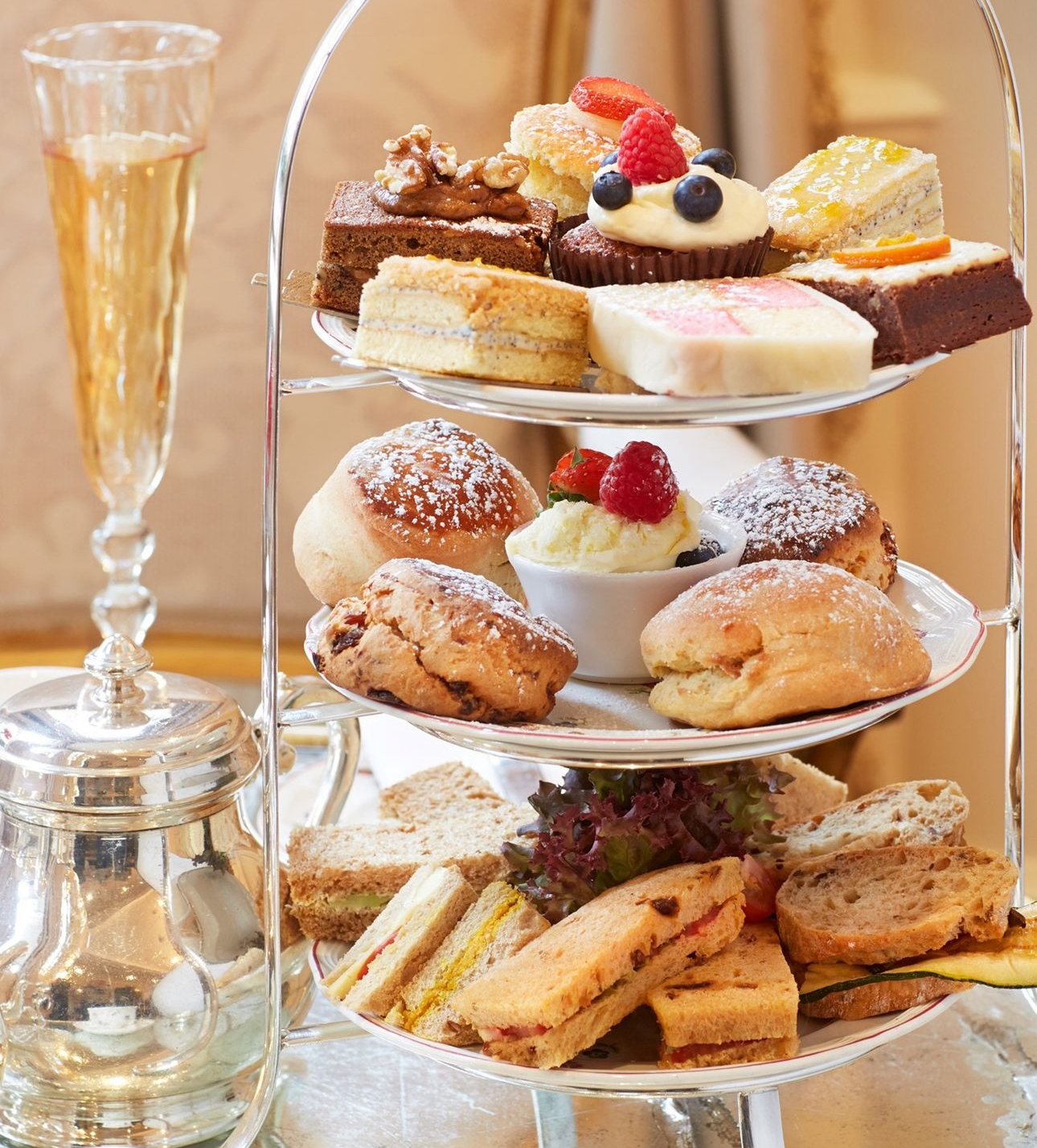 a three tier tray of vegan afternoon tea desserts, scones, and sandwiches