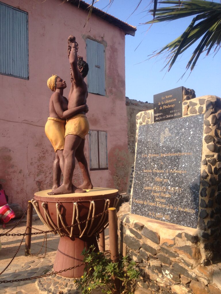 scultupre depicts a dark skinned man and woman standing on a djembe freedom drum. Man raised his hands up in a victory motion while the woman is holding on to the man's waist. 