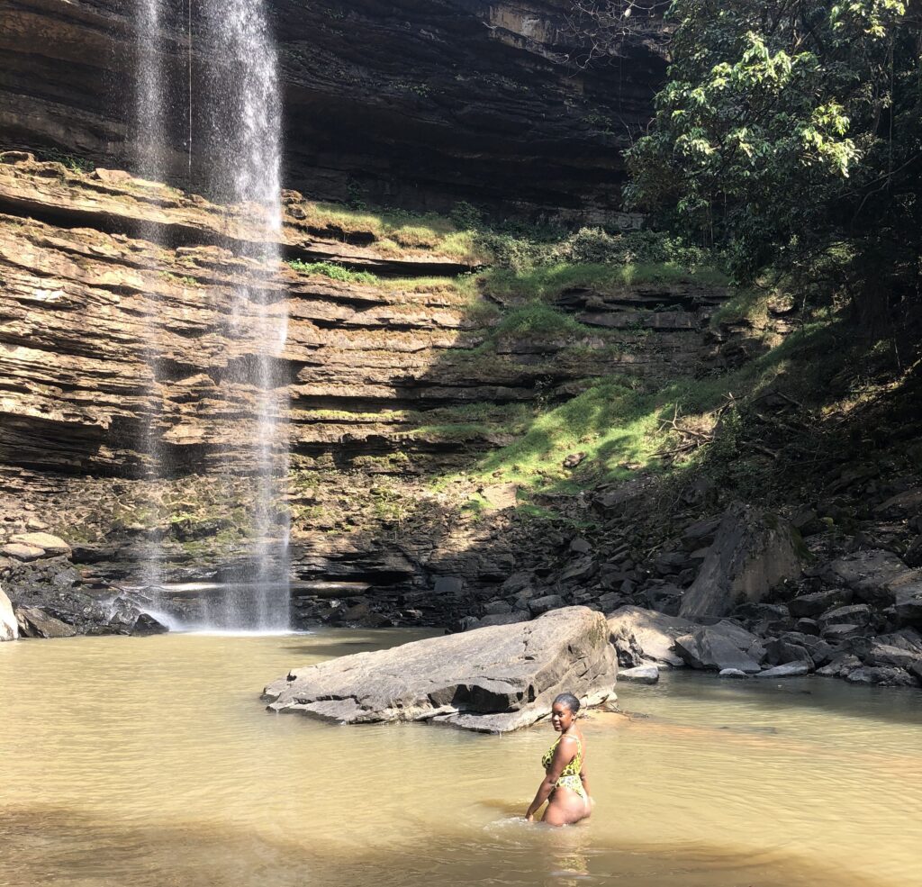 Black woman in yellow bathing suit standing in front of Boti Waterfalls