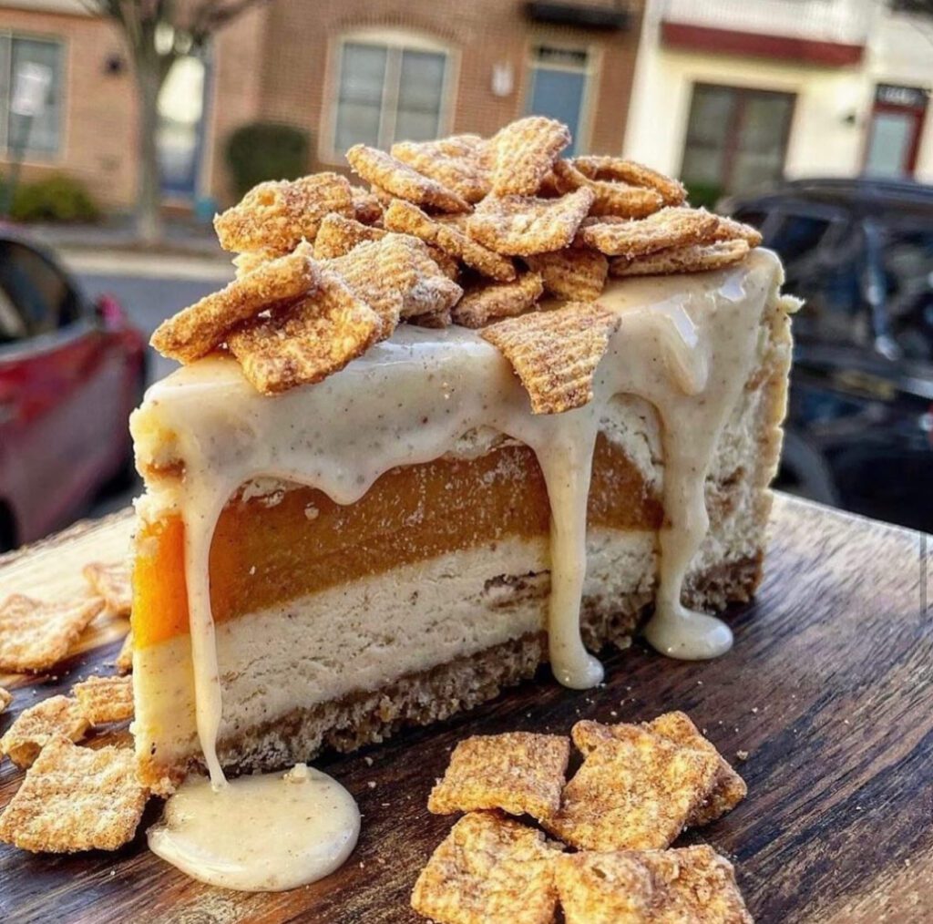 cheesecake / cake with cinnamon crunch cereal on the top and white sauce dripping along side the slice of cake