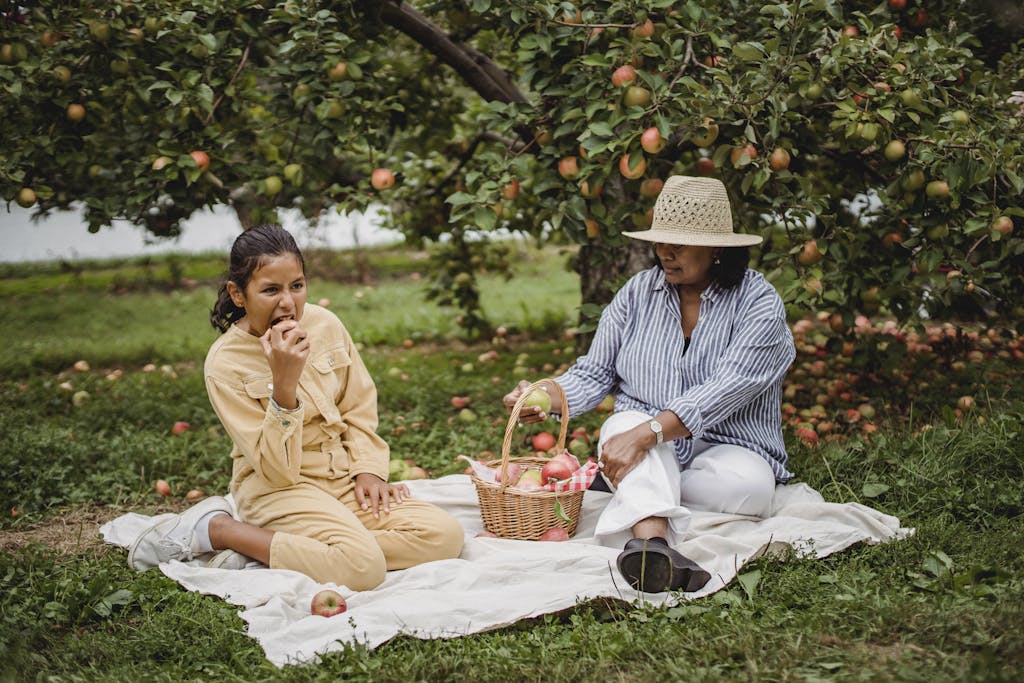 Ethnic mother and daughter having picnic under tree branches